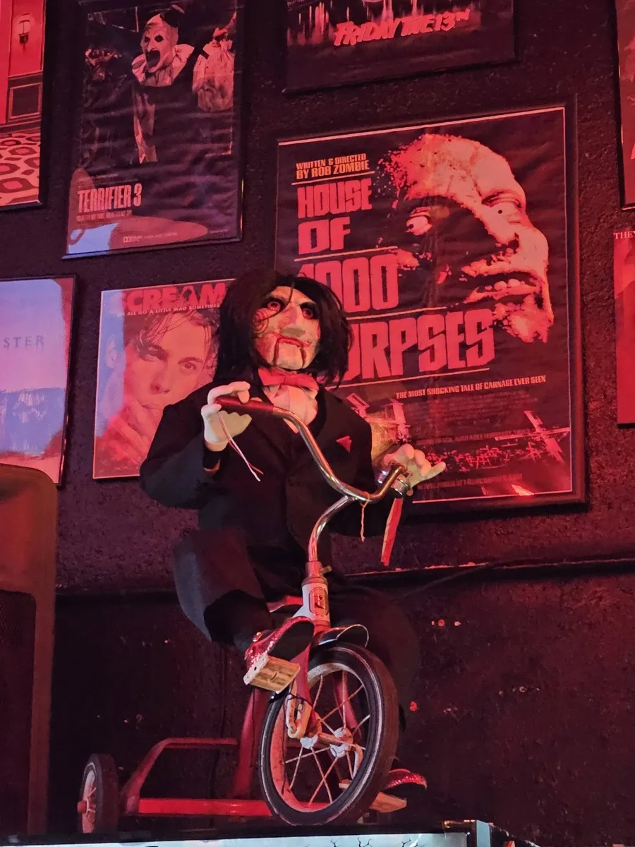 Jigsaw puppet on tricycle with horror movie posters